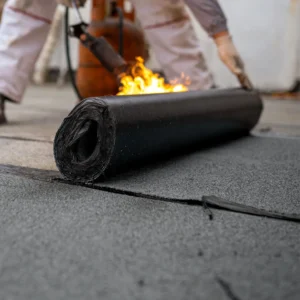 Worker applying torch-on roofing membrane with flame
